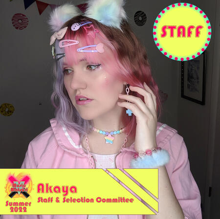 Akaya, a white person with light pink and purple hair wearing many clips and accessories and a pink jacket.